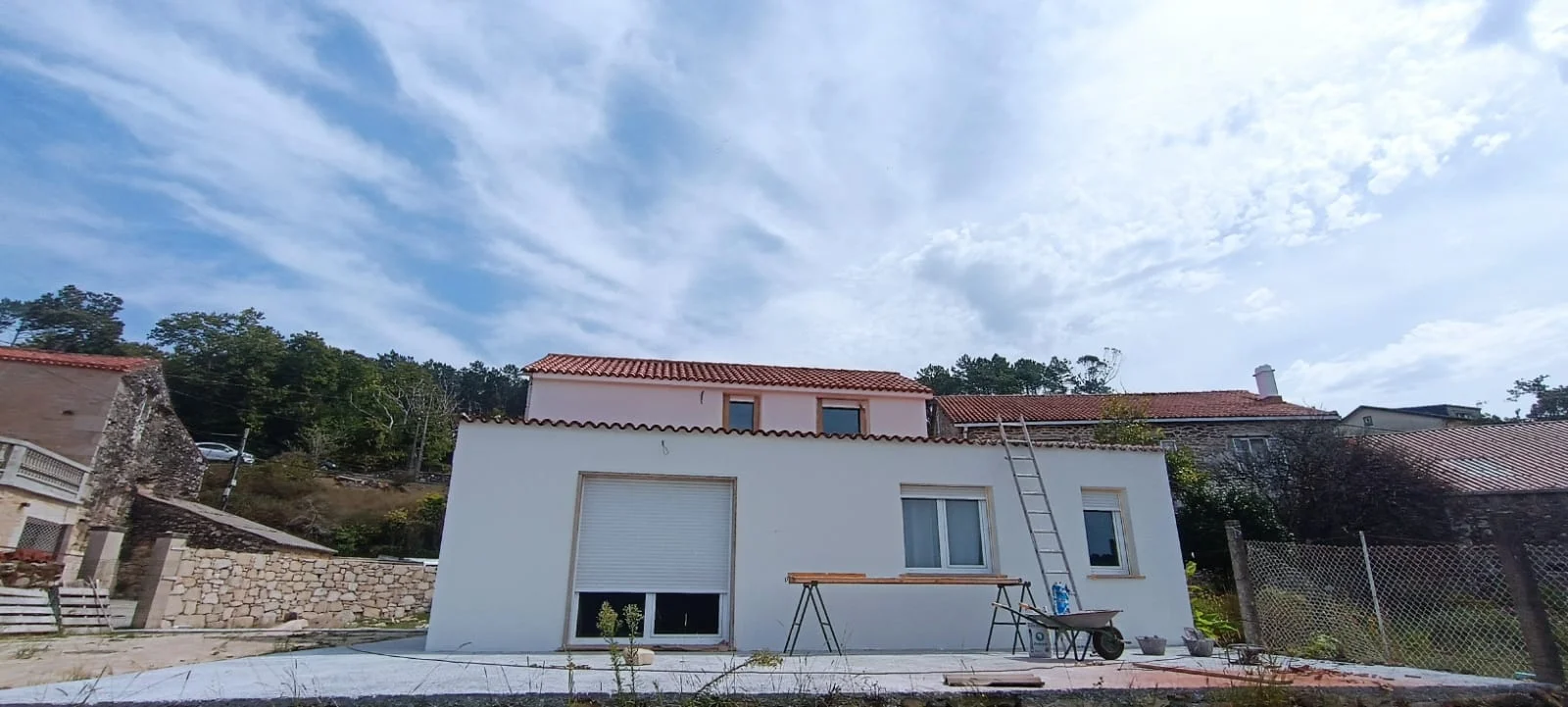 Vista general del exterior. Frente de la vivienda con acabado blanco, ventanas protegidas y medios auxiliares todavía en la zona de obra.